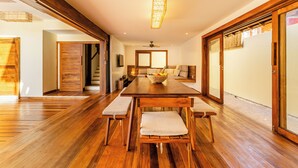Un vaste espace dédié à la salle à manger, avec une table et des bancs en bois, un ventilateur de plafond et une grande fenêtre qui laisse entrer la lumière naturelle.