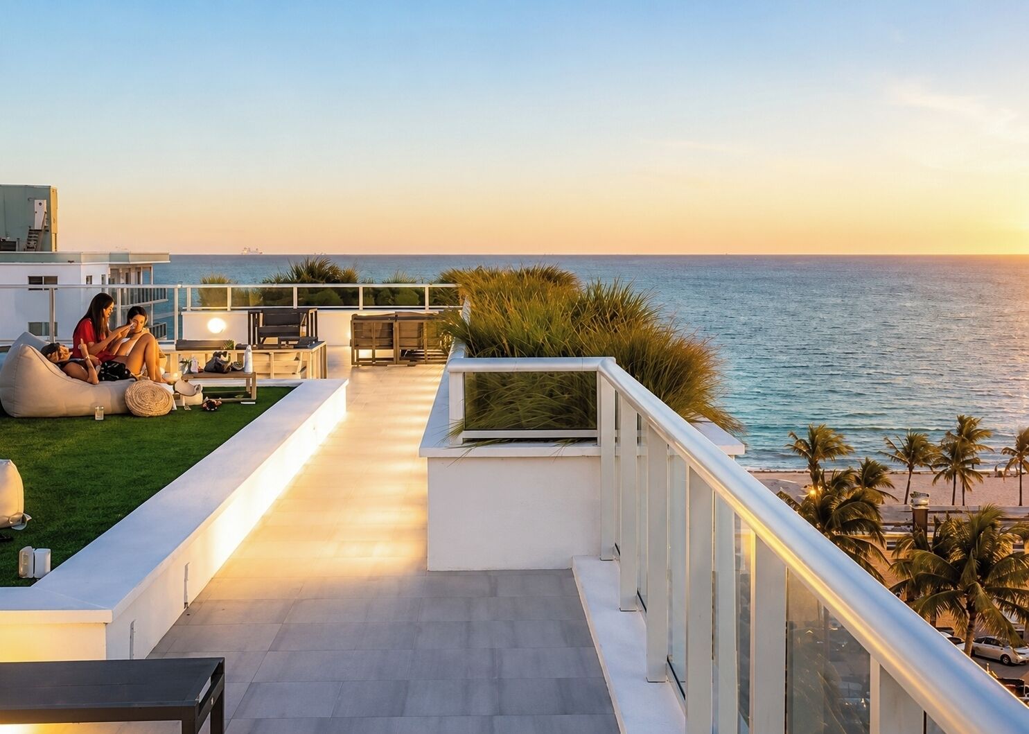 A rooftop terrace with a view of the ocean, seating areas, and a glass balustrade.
