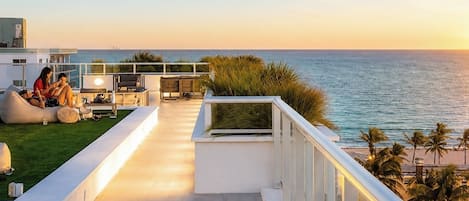 A rooftop terrace with a view of the ocean, seating areas, and a glass balustrade.