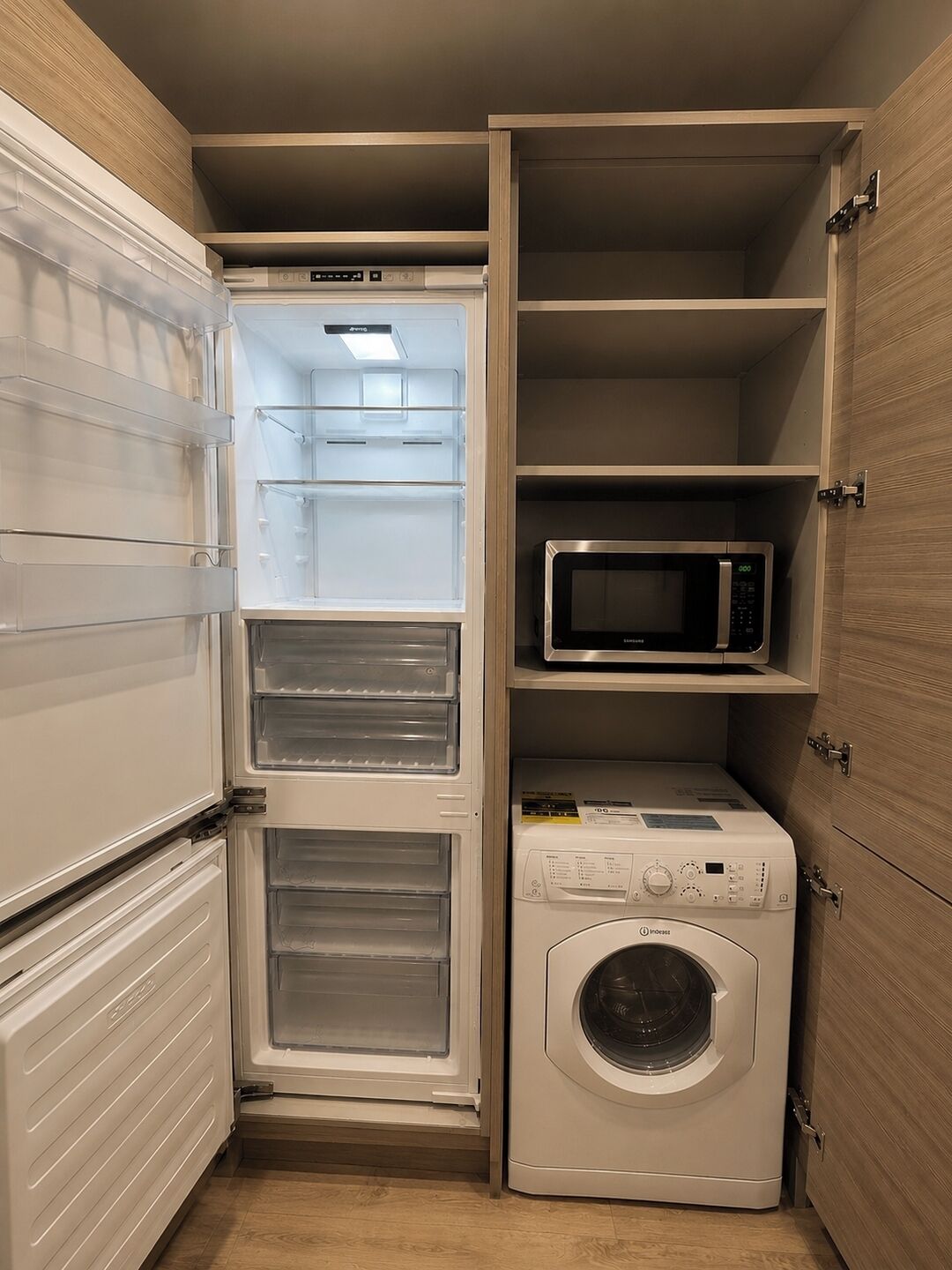 A compact kitchen with a built-in refrigerator, microwave, and washing machine.