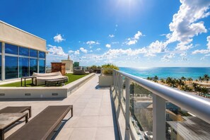 Terraço no telhado com área de estar externa, vista para o oceano e céu claro.