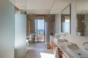Enjoy a serene atmosphere in this bathroom with a large sink and spacious mirror, opening up to a balcony with ocean views.