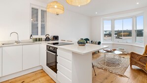 Una cucina moderna con mobili bianchi, un'isola centrale e un'area pranzo con una sedia e un tavolo in vimini.