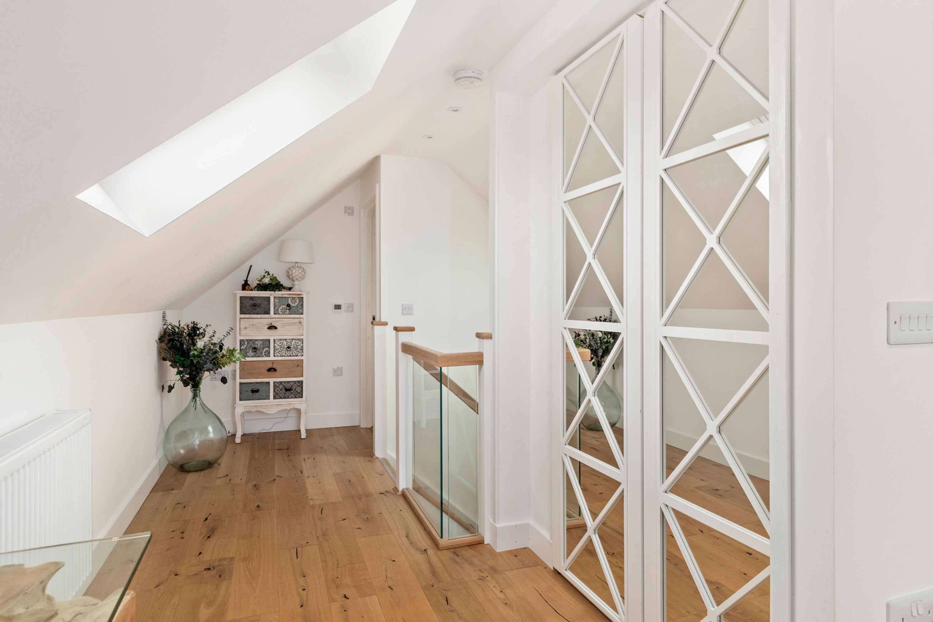 A modern interior with a sloped ceiling, wooden flooring, a glass door with a geometric pattern, and a white wall with a built-in shelf.