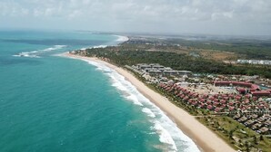 Oversigtsbillede af et kystområde med en strand, et resort med flere bygninger, og et skovområde i baggrunden.