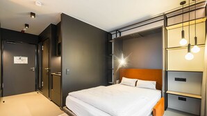 Una habitación de hotel moderna con una cama grande, armario empotrado y una lámpara de diseño sobre la cama.