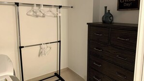 A closet with a metal rod rack holding clothes, a dark wooden dresser with drawers, and a motivational quote on the wall. - Monthly Luxury Loft - Old Town (Fort Collins)