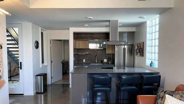 A modern kitchen with a central island, stainless steel appliances, and a bar seating area with chairs. - Monthly Luxury Loft - Old Town (Fort Collins)