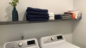 A laundry area with two white LG Direct Drive washing machines, a shelf with folded towels and a decorative vase. - Monthly Luxury Loft - Old Town (Fort Collins)