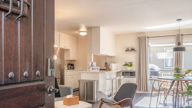 A modern kitchen with white cabinets, a stainless steel refrigerator, and a dining area with a table and chairs. - Modern Carmel Unit - Central, Big Yard & Fire Pit! (Carmel-by-the-Sea)