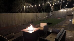 An outdoor patio area with a fire pit, wicker furniture, and string lights. - Modern Carmel Unit - Central, Big Yard & Fire Pit! (Carmel-by-the-Sea)