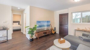 A modern living room with a large TV, a guitar, and a plant. - Modern Carmel Unit - Central, Big Yard & Fire Pit! (Carmel-by-the-Sea)