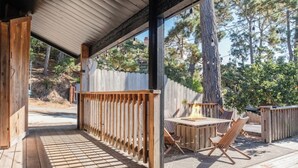 Una terraza de madera con un brasero y zona de estar, rodeada por una valla de madera y árboles.