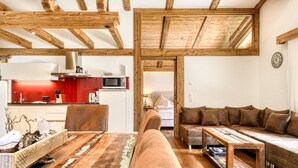 A cozy living room with a wooden ceiling, a red kitchen in the background, and a brown sofa with cushions. - Dahoam Appartments 3-zimmer mit Balkon Loisch (Buerserberg)