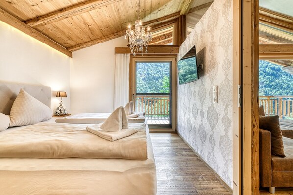 A bedroom with a large bed, a chandelier, a television, and a balcony with a wooden railing.
