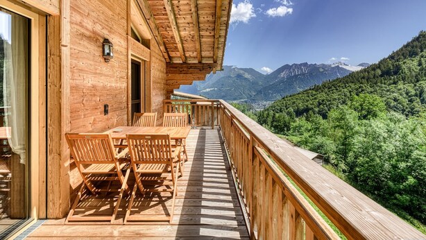 A wooden deck with a table and chairs, overlooking a mountainous landscape. - Dahoam Appartments 3-zimmer mit Balkon Loisch (Buerserberg)