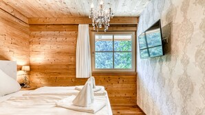 Un dormitorio con paneles de madera, una cama, una araña, una ventana y un televisor montado en la pared.