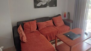 A living room with a dark grey sofa, orange cushions, a wooden coffee table, and a black and white flower painting on the wall. - 2 Bed Apt-easy Access to Pool-mar Menor Nearby (San Javier)