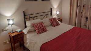 A neatly made bed with a red blanket, two patterned pillows, a bedside lamp, and a nightstand with a book and remote control. - 2 Bed Apt-easy Access to Pool-mar Menor Nearby (San Javier)