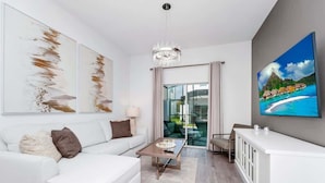 Ein modernes Wohnzimmer mit einem weißen Sofa, einem Couchtisch und einem großen Gemälde, das einen tropischen Strand zeigt.