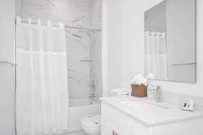 A modern bathroom with a shower curtain, a bathtub, a toilet, and a sink with a mirror. - Family 5BR Retreat Near Disney + Pool (Davenport)