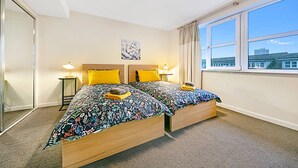 A double bed with floral bedding, two bedside lamps, a mirror, and a window with a city view. - Bannermill Place Apartment | Grampian Lettings Ltd (Aberdeen)