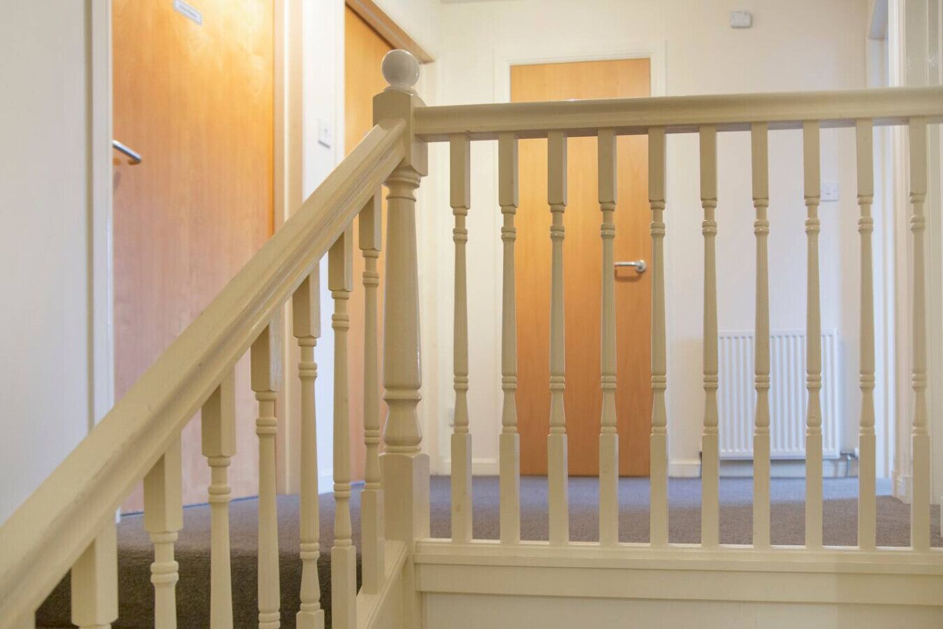 A staircase with a white balustrade leading to a room with a wooden door and a radiator.