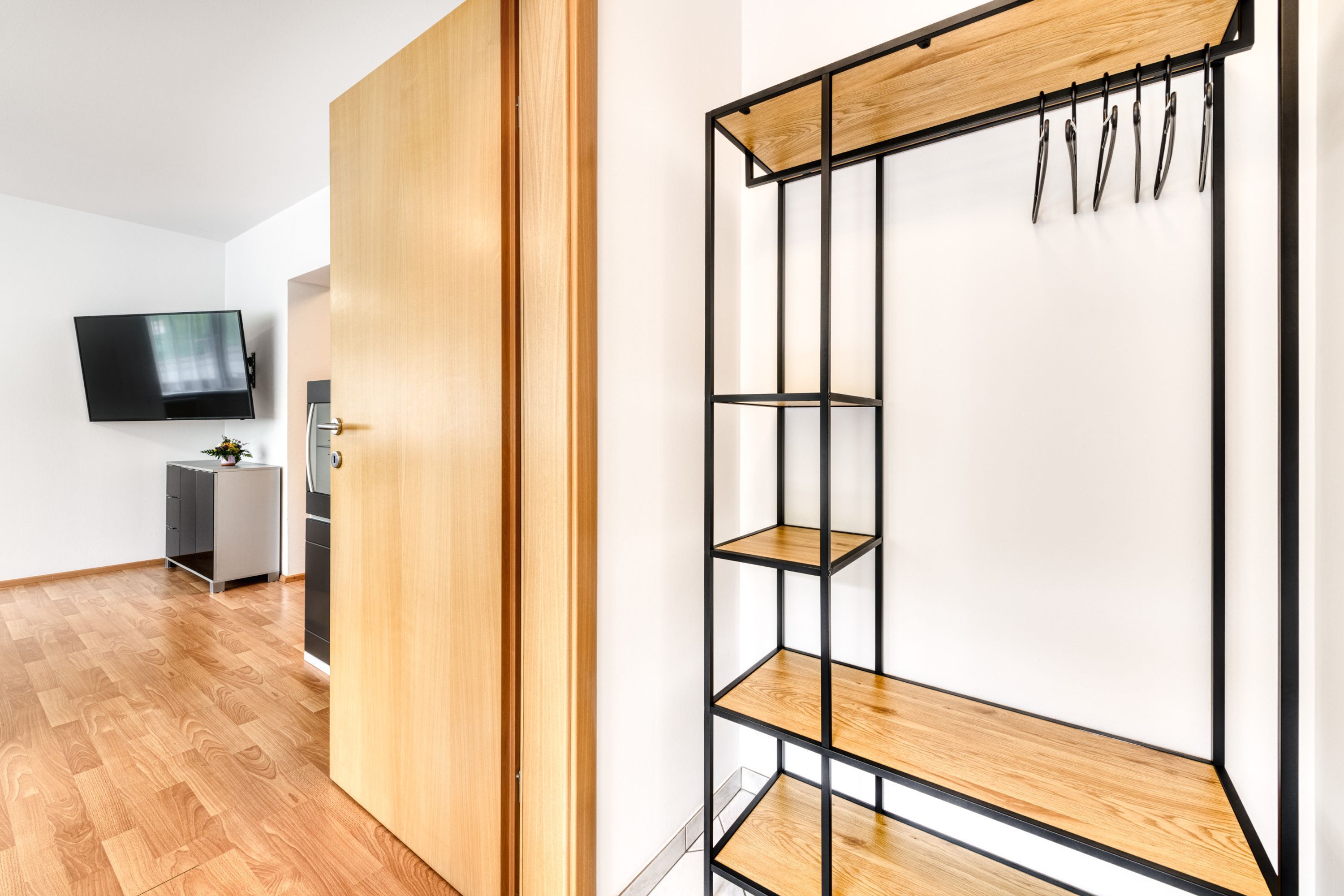 A modern room with a wooden floor, a wardrobe, a TV, and a metal shelving unit with hooks.
