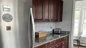 A modern kitchen with dark wood cabinets, a stainless steel refrigerator, a granite countertop, and a toaster. - Charming 2-bedroom apartment with WiFi, AC in downtown Bar Harbor (Bar Harbor)