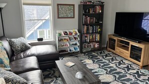 A living room with a leather sofa, a coffee table, a bookshelf, and a television. - Charming 2-bedroom apartment with WiFi, AC in downtown Bar Harbor (Bar Harbor)