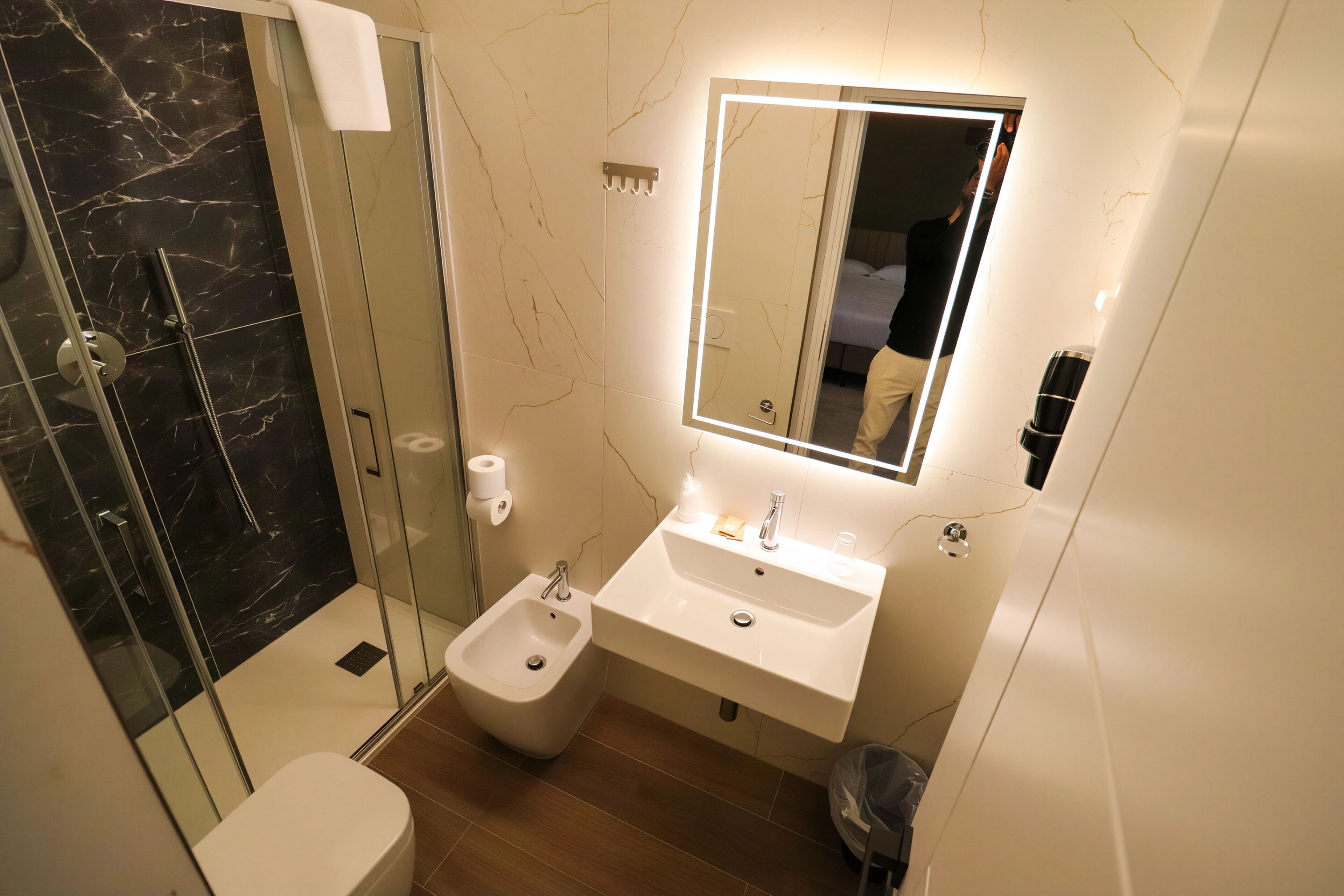 A modern bathroom with a glass-enclosed shower, a bidet, a sink with a mirror, and a toilet.