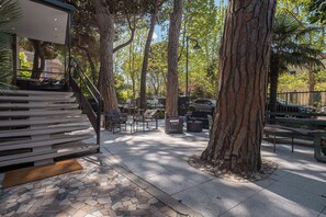 Un patio al aire libre con suelo de baldosas de piedra, bancos de madera y una zona de estar con sillas y una mesa.