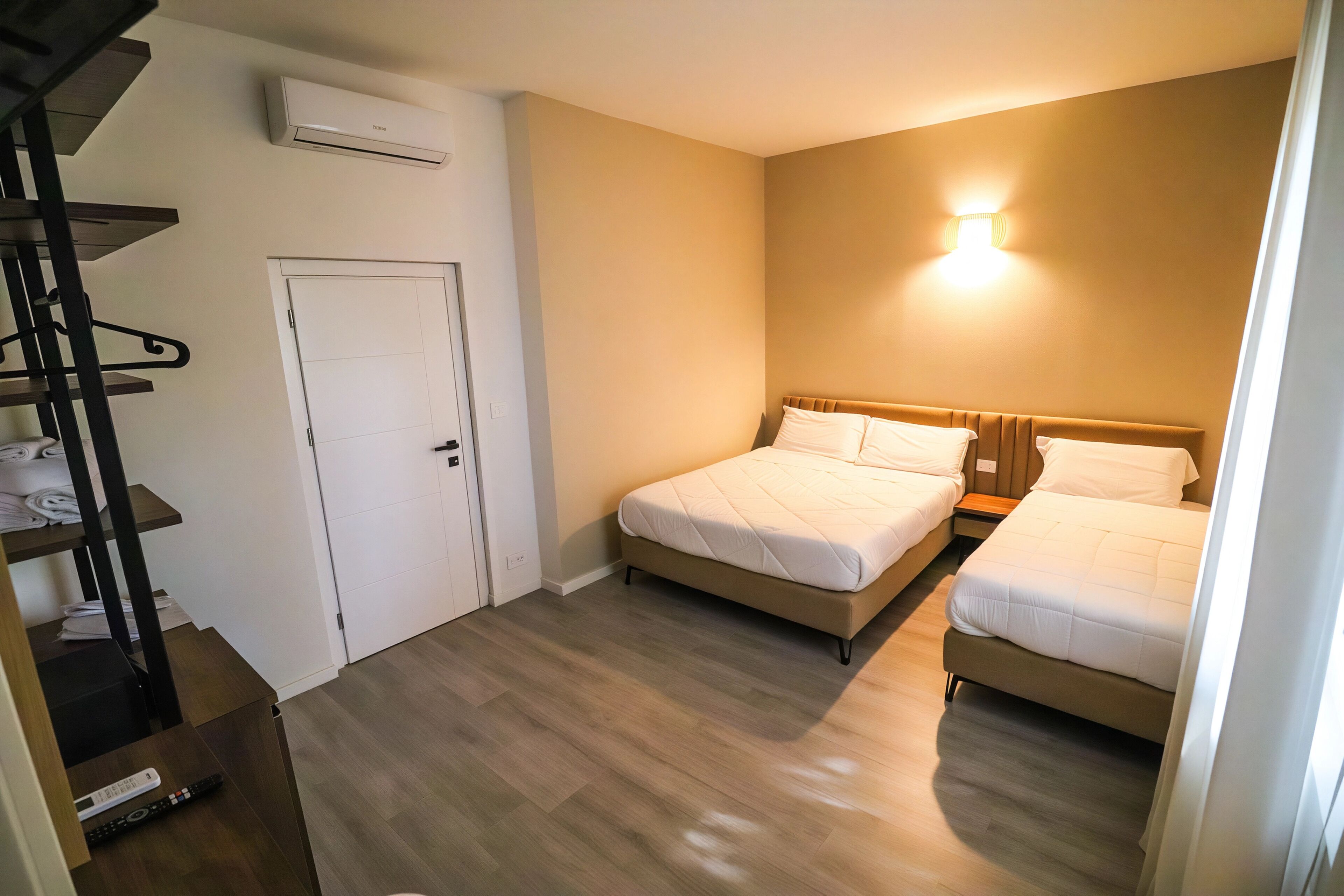 A bedroom with two beds, a wardrobe, a staircase, and an air conditioning unit.