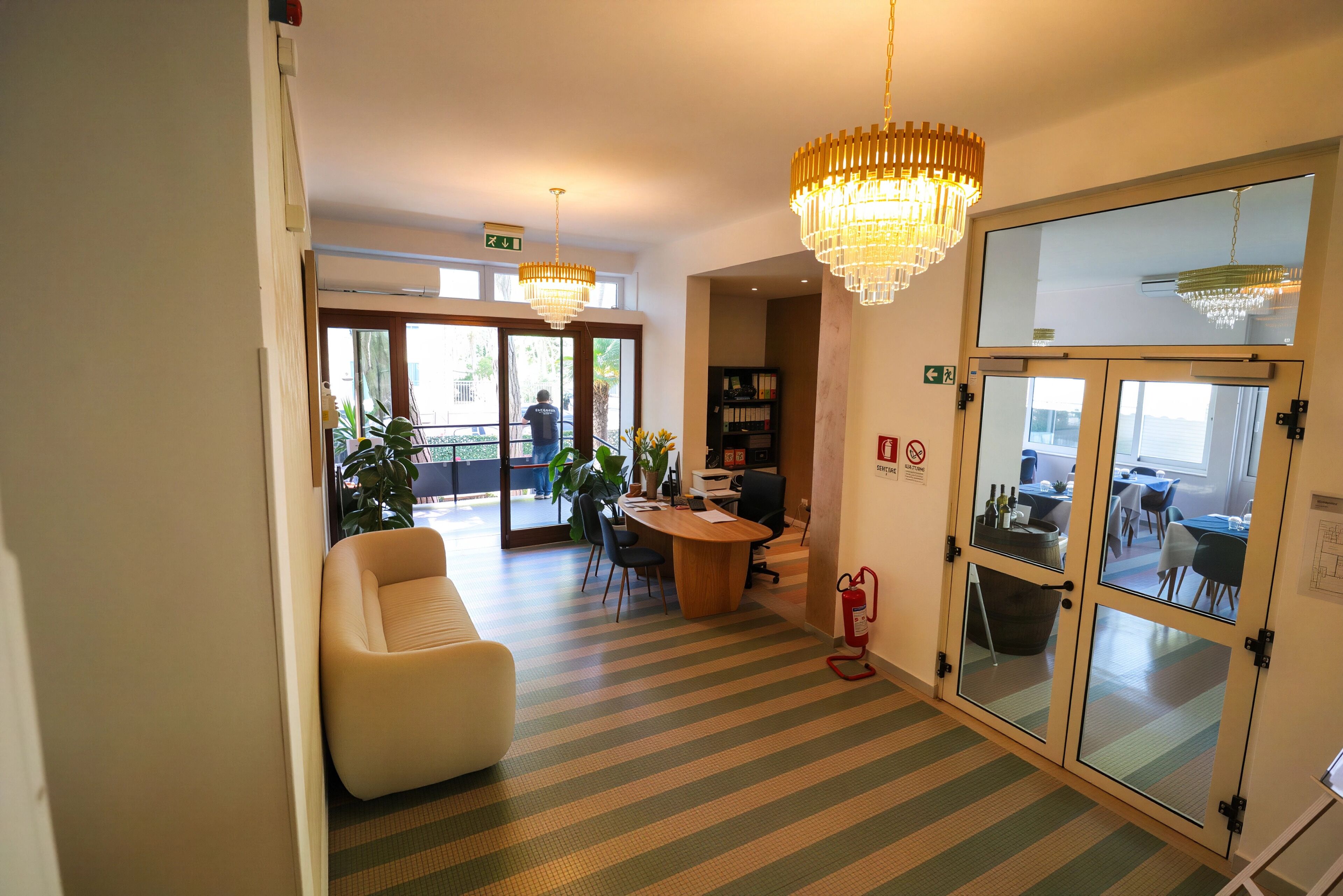 A hotel lobby with striped flooring, a reception desk, a seating area, and a large mirror.