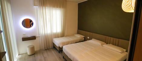 A hotel room with two beds, a round mirror, a bedside table, a small stool, and a wall-mounted light fixture.