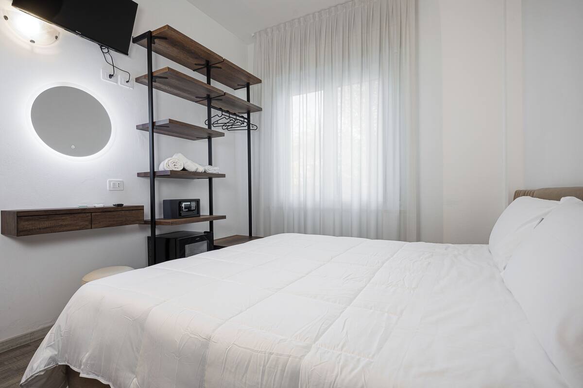 Une chambre d’hôtel moderne dotée d’un grand lit, d’un téléviseur fixé au mur, d’un miroir rond et d’étagères intégrées, ainsi que d’un micro-ondes et d’une petite table.