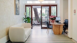 Een modern interieur met een bank, een houten bureau en een groot raam met uitzicht op bomen en gebouwen.