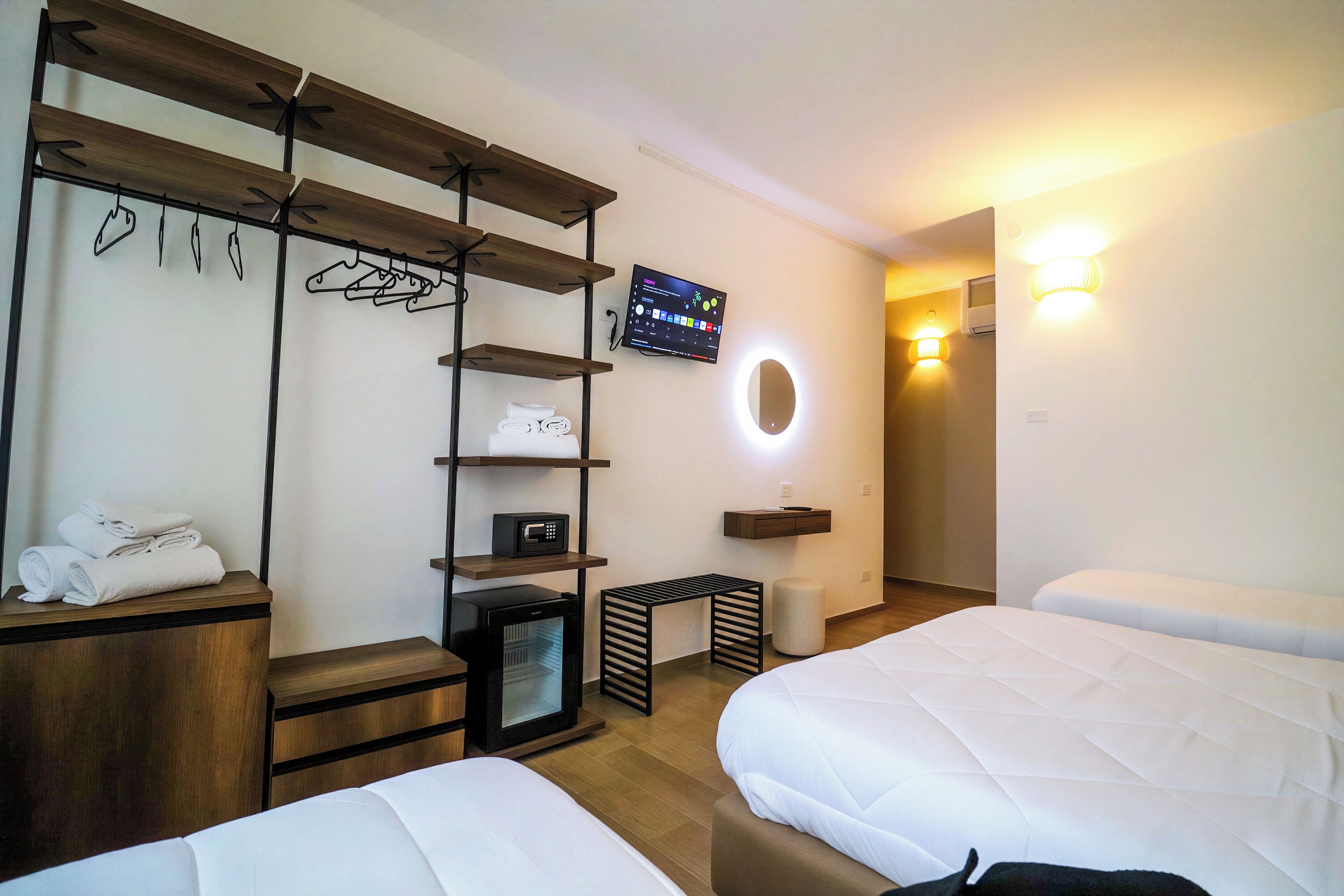 Una camera d'albergo con due letti, una televisione, uno scaffale con asciugamani e un tavolino.