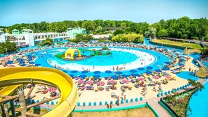 Een waterpark met meerdere zwembaden, een grote gele glijbaan en tal van strandparasols.