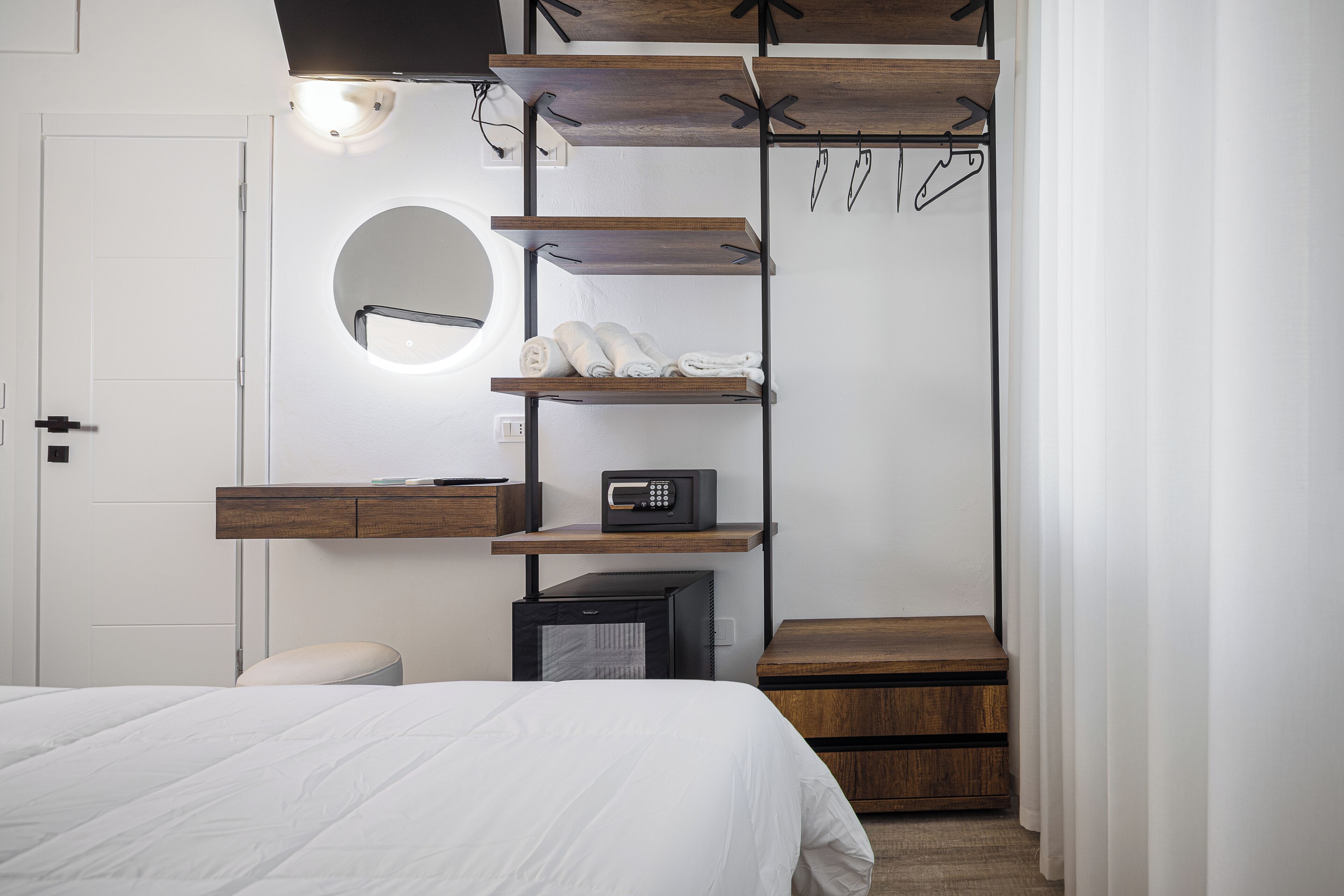 A bedroom with a bed, a built-in wardrobe with shelves, a round mirror, and a microwave.