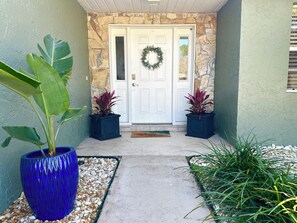 Entrada de una casa con un muro de piedra, una puerta blanca y dos macetas con plantas.