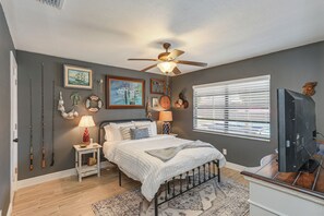 A bedroom with a bed, bedside lamps, a ceiling fan, a TV, and a window with blinds. - The SALTY PALM Coastal Retreat, sleeps 13! Resort-Inspired POOL & Themed Rooms (Palm Bay)