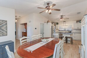 A dining area with a wooden table, white chairs, and ceiling fans. - The SALTY PALM Coastal Retreat, sleeps 13! Resort-Inspired POOL & Themed Rooms (Palm Bay)