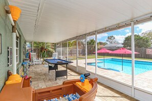 A covered outdoor area with a pool, a foosball table, and a ping pong table. - The SALTY PALM Coastal Retreat, sleeps 13! Resort-Inspired POOL & Themed Rooms (Palm Bay)