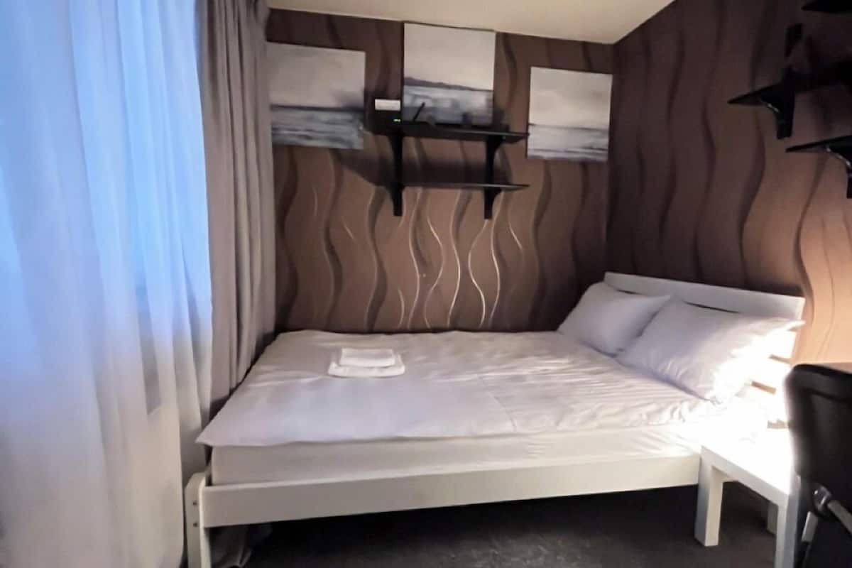 A hotel room with a bed, a bedside table, a chair, and a wall-mounted TV.