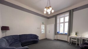 Una habitación con un sofá azul oscuro, un escritorio blanco, una silla y un ventanal grande.