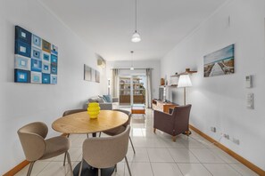 Un salon moderne avec une table à manger ronde, des chaises, un canapé, un téléviseur et des œuvres d’art accrochées aux murs.