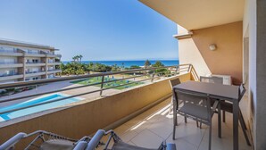 Un balcone con piscina, tavolo e sedie, con vista su una spiaggia e un edificio.
