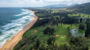 A coastal golf course with a beach, green fairways, and a water hazard.