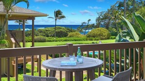 A wooden deck with two wicker chairs and a round table, overlooking a lush garden and the ocean.